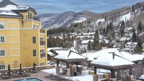 A resort with a pool, outdoor seating, and snow-covered mountains in the background. - Ritz Carlton Vail #314 3 Bedroom Condo (Vail)