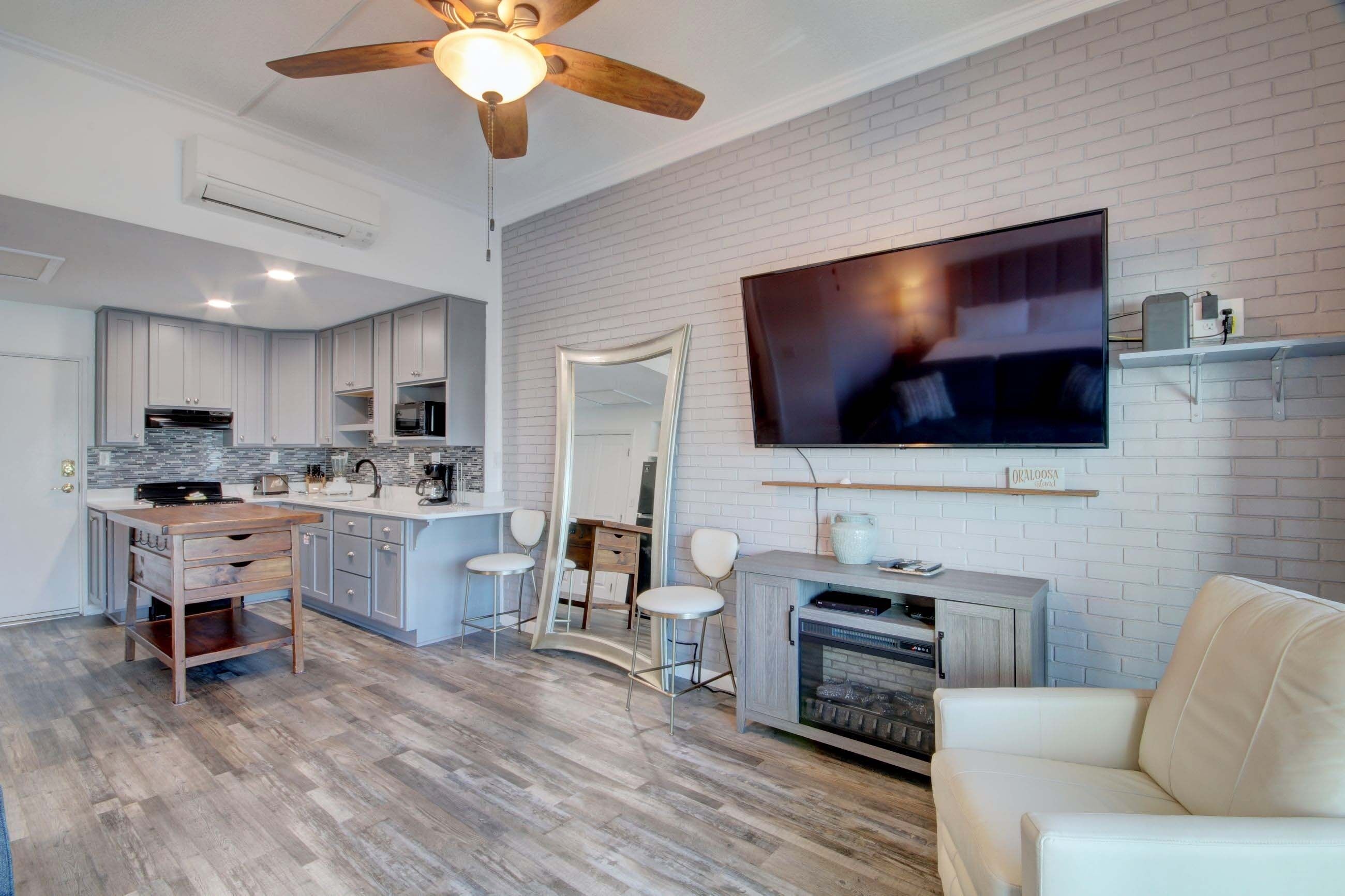 A modern kitchen with white cabinets, a wooden island, and a large flat-screen TV mounted on a brick wall.