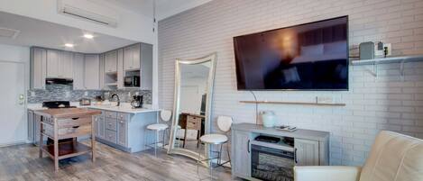 A modern kitchen with white cabinets, a wooden island, and a large flat-screen TV mounted on a brick wall.