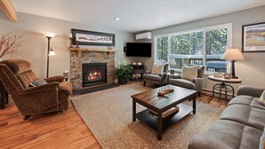 A living room with a fireplace, a sofa, a coffee table, and a TV mounted on the wall. - 8 East Butte Ln 3 Bedroom Home (Bend)