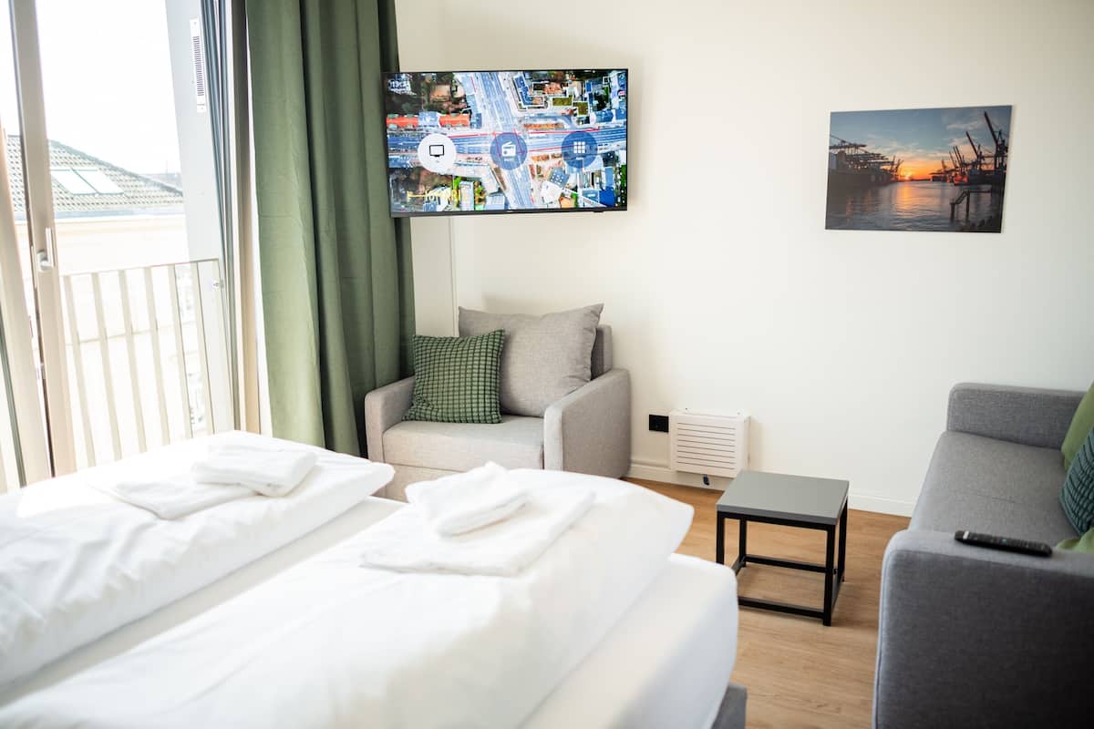 A hotel room with a bed, a chair, a small table, a TV, and a painting on the wall.