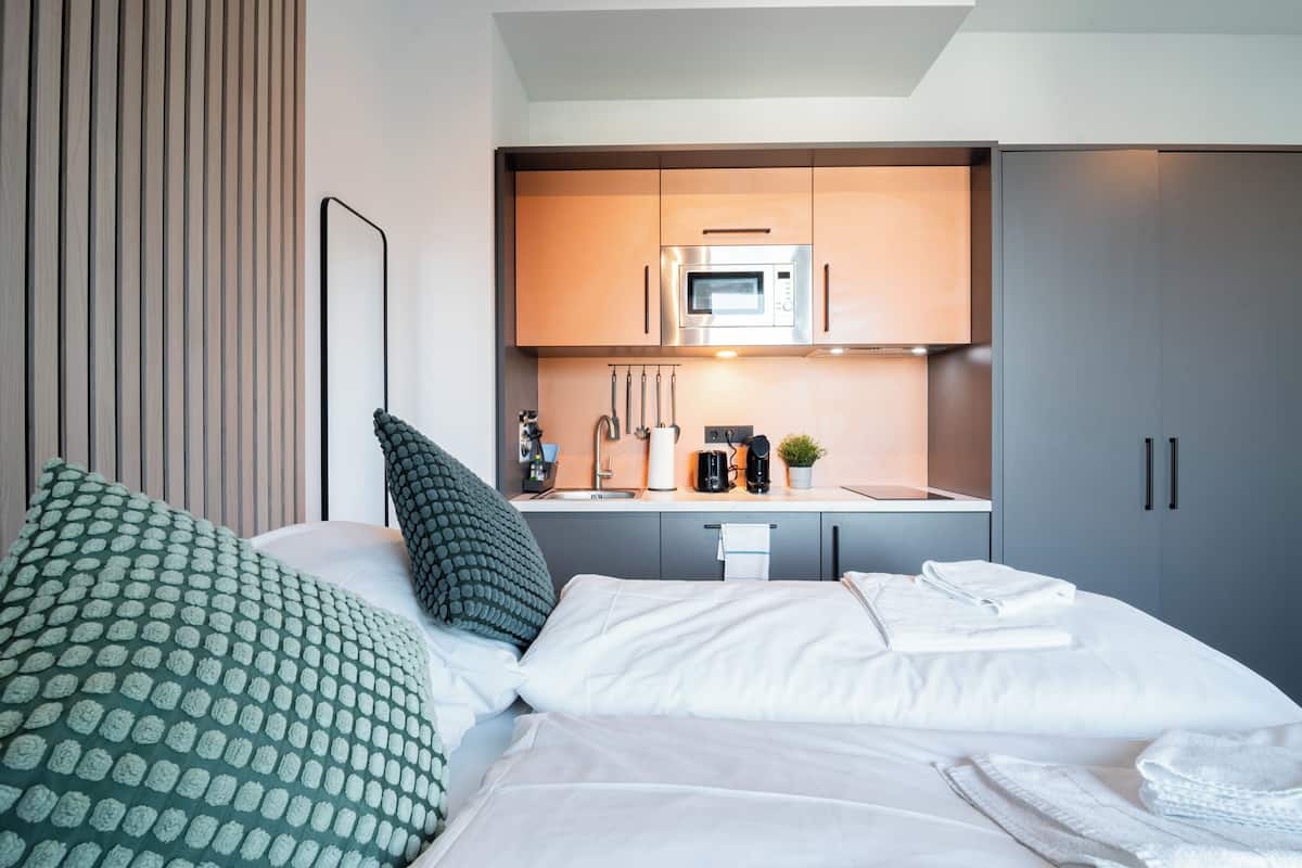 A modern hotel room with a bed, a kitchenette, and a bathroom.