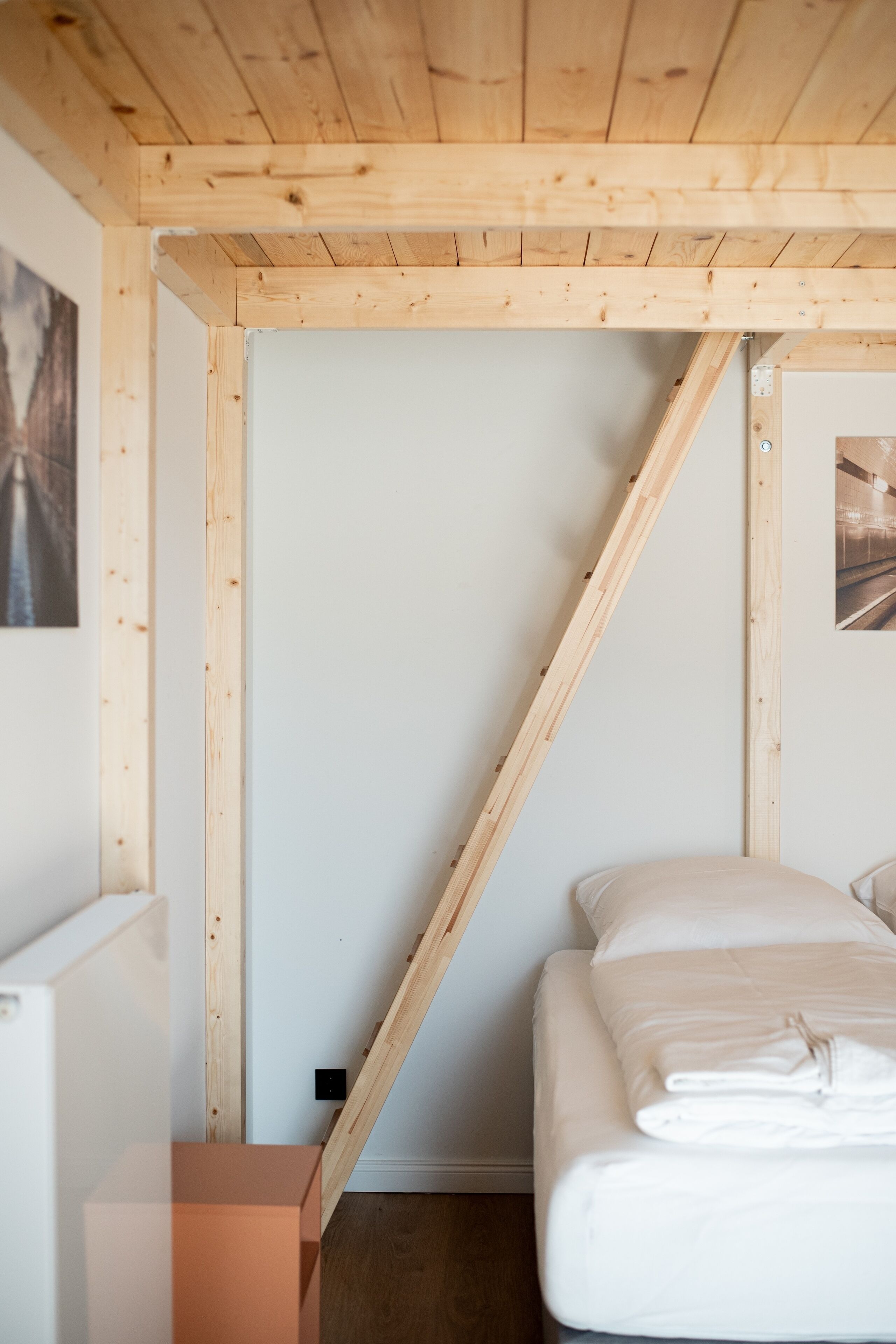 Un dormitorio con techo inclinado, una cama con ropa de cama blanca, cabecero de madera y una mesita de noche pequeña.