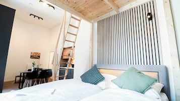 A bedroom with a bed, pillows, a desk with chairs, a ladder, and a sloped ceiling.
