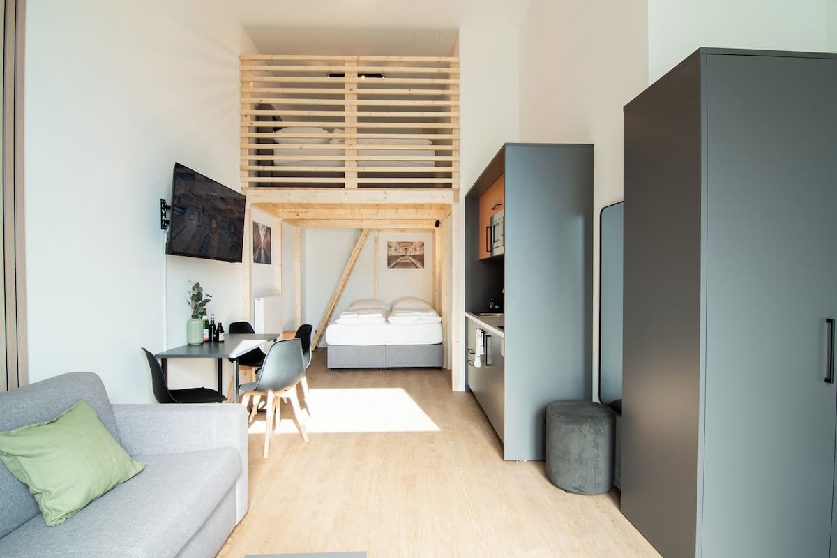 A compact, modern living space with a loft bedroom, a kitchenette, and a dining area.