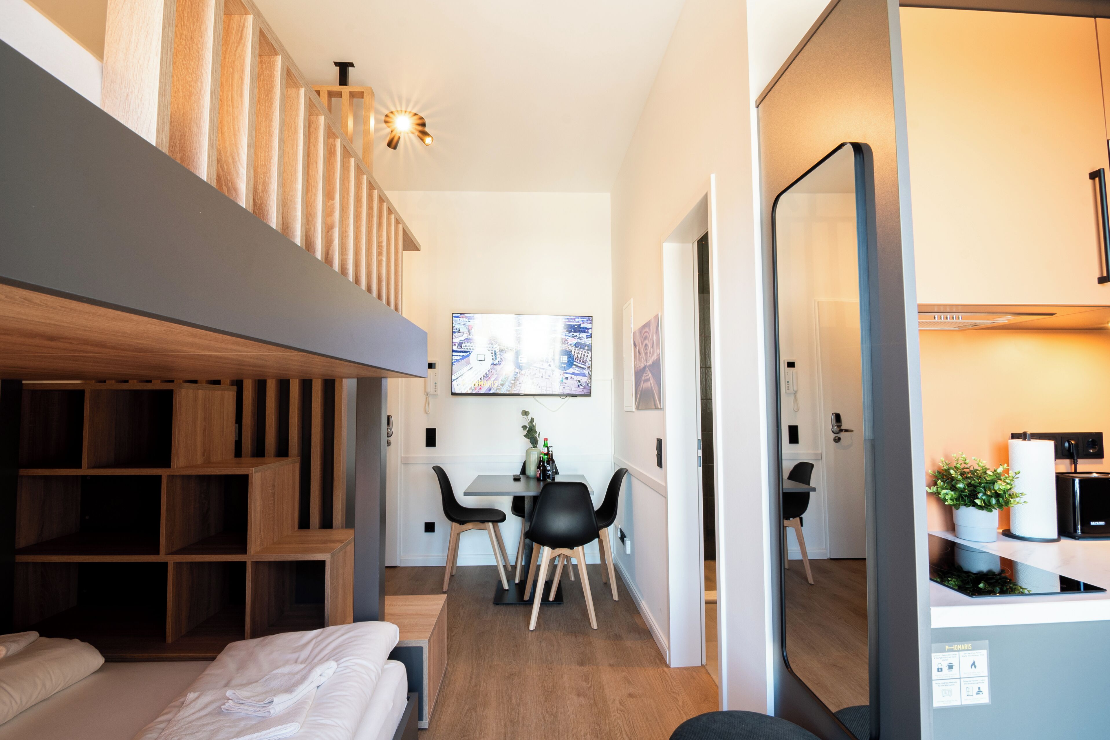 Una habitación de hotel moderna con cama estilo loft, zona de comedor con televisor y cocina.