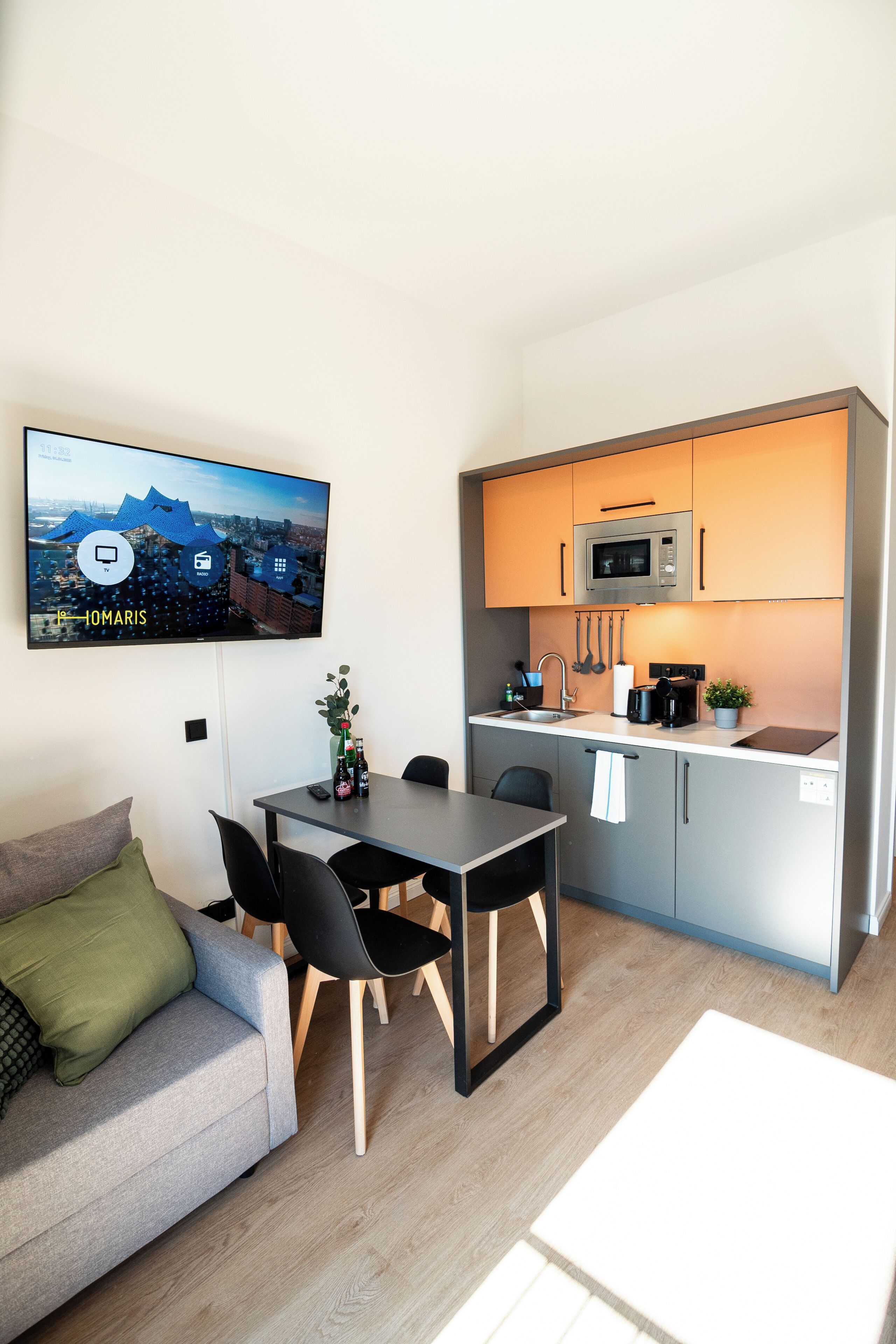 Ett kompakt bostadsutrymme med en matplats, ett litet kök och en tv som är monterad på väggen och visar en stadsbild.