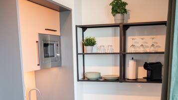 Eine kleine Küche mit integriertem Mikrowellenherd, Spüle und kompaktem Kühlschrank. Über der Spüle befindet sich ein Regal mit Gläsern und einem Blumentopf.