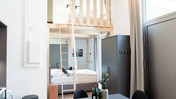 Una habitación moderna y compacta con una cama litera, una zona de comedor con mesa y sillas, un sofá y una kitchenette.