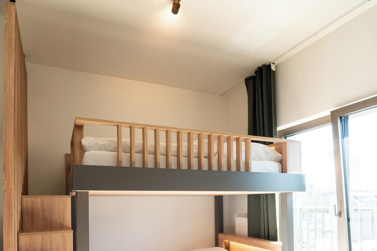 A modern room with a bunk bed, wooden staircase, and a table.