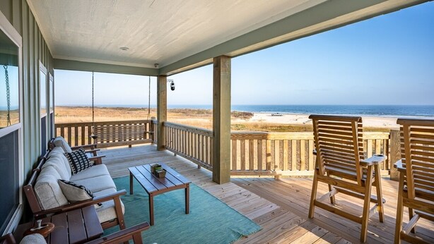 A covered deck with a view of the beach, wooden furniture, and a swing. - Perfectly Happy 4 Bedroom Home (Port Bolivar)