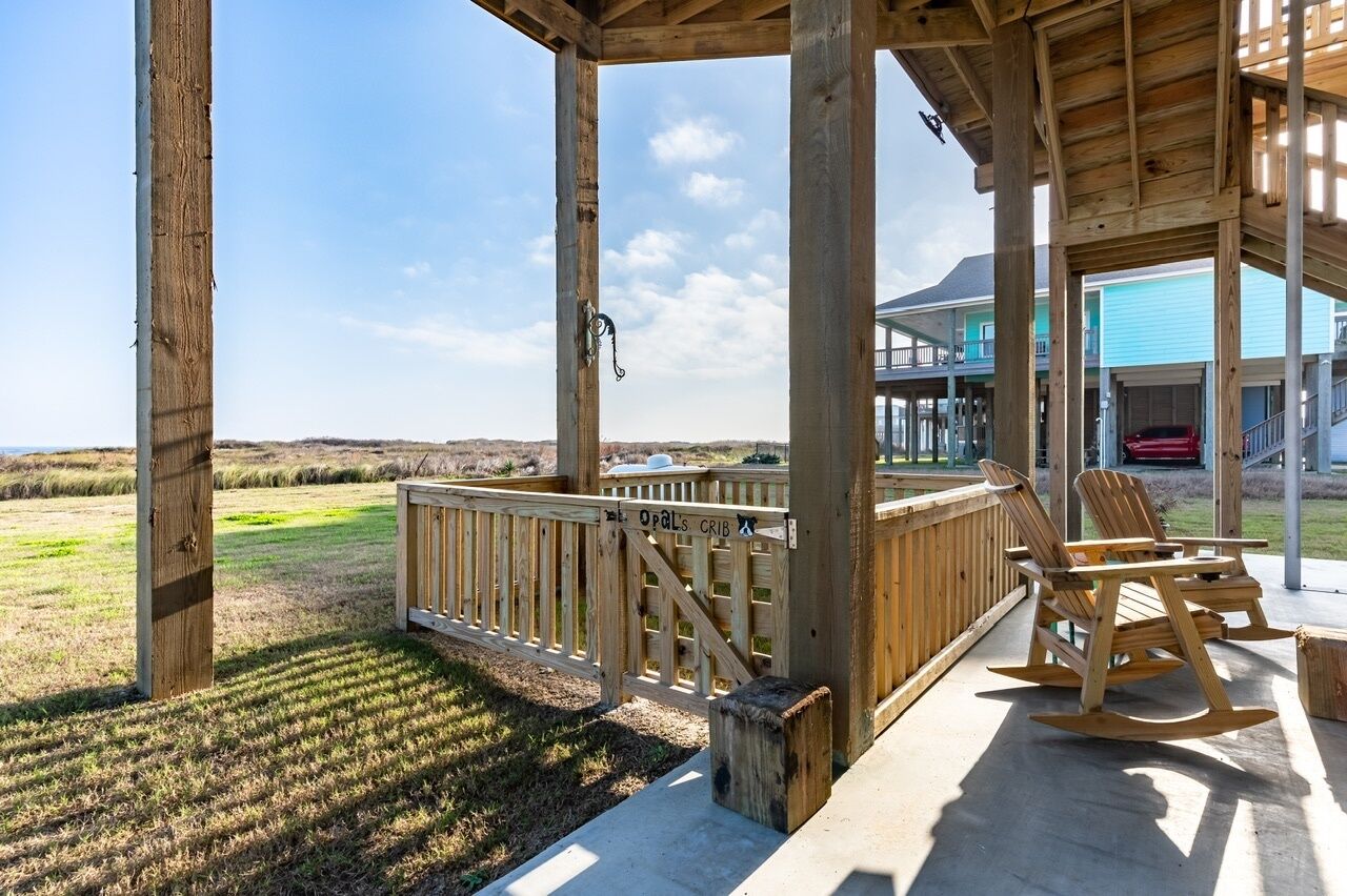 A wooden deck with a view of the beach, a wooden chair, and a sign reading "Opal's Crib".