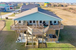 A two-story house with a balcony and a deck, surrounded by a grassy area and other houses. - Perfectly Happy 4 Bedroom Home (Port Bolivar)