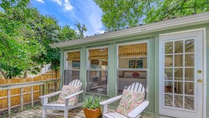 Une terrasse extérieure couverte, avec deux chaises Adirondack blanches et une plante en pot.