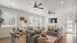 A modern living room with grey sofas, a wooden coffee table, and a kitchen area with a cabinet and countertop. - Beech Bungalow 5 Bedroom Townhouse (St. George)