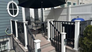 A covered outdoor patio with a table and chairs, a black umbrella, and a blue barbecue grill.