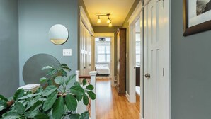 A hallway with a wooden floor, a round mirror, and a potted plant.