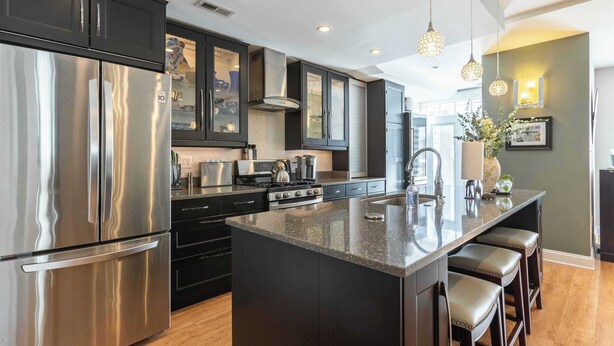A modern kitchen with stainless steel appliances, dark cabinetry, and a central island with bar stools.
