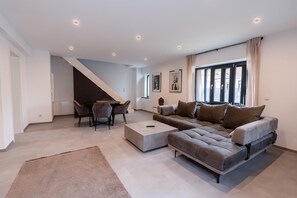 A spacious living room with a grey sectional sofa, a coffee table, and a dining area with a table and chairs.