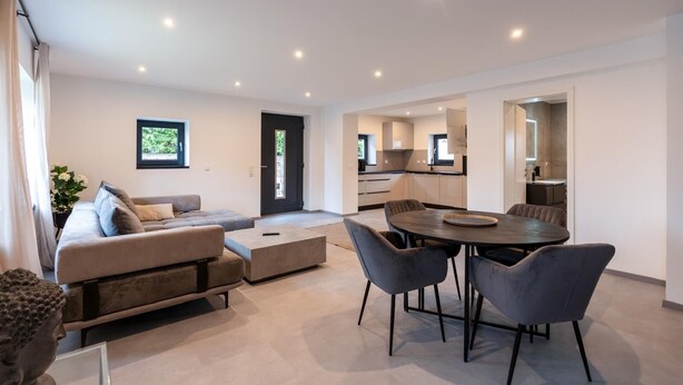 A modern living room with a sofa, a dining table with chairs, and a kitchen in the background. - Welcome to your dream vacation home! (Eldetal)
