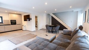 A modern living room with a grey sofa, a dining table with chairs, and a kitchen area with cabinets and appliances. - Welcome to your dream vacation home! (Eldetal)