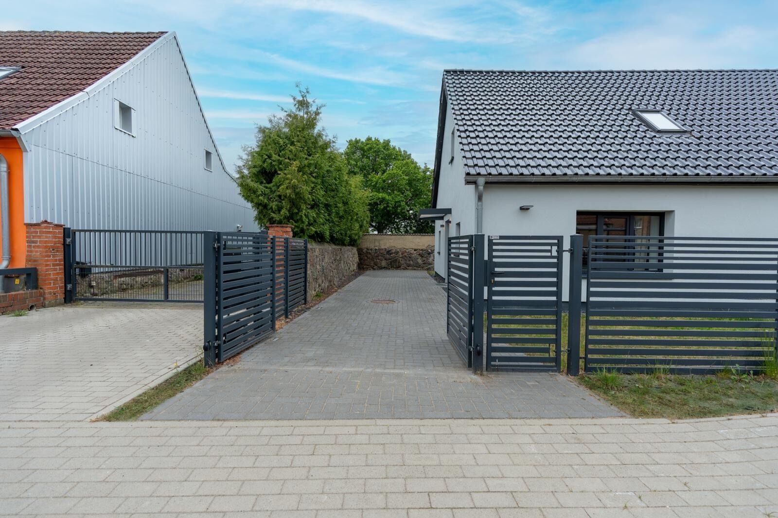 A gated driveway leading to a residential area with a modern house and a garage.