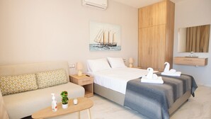 Una habitación de hotel moderna con una cama, un sofá, una pequeña mesa con servicios, un cuadro de un velero y un armario de madera.