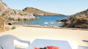 Una mesa con mantel blanco y dos rebanadas de sandía, con vista a una costa rocosa y una vista despejada del mar.