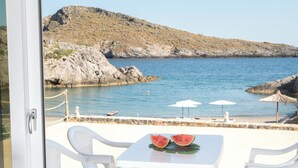 Una terraza con sillas y mesa blancos, con vista a un litoral rocoso y un mar tranquilo.