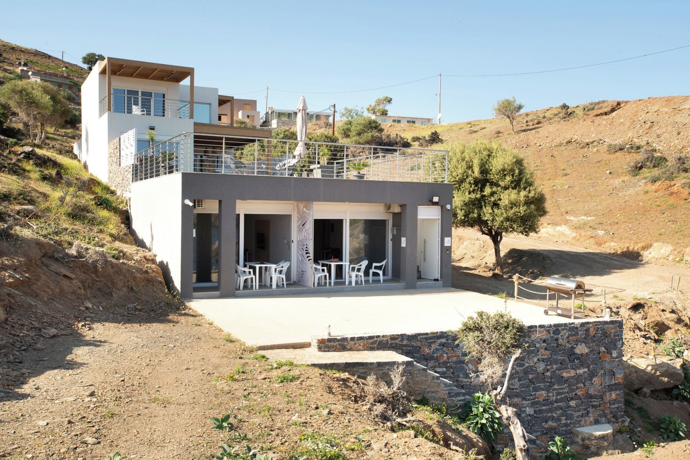 Una casa moderna de dos pisos, con balcón, zona de estar exterior y pared de piedra.