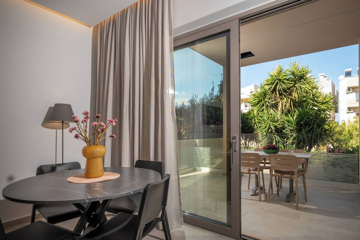 A modern dining area with a round table, chairs, a vase with flowers, and a lamp.