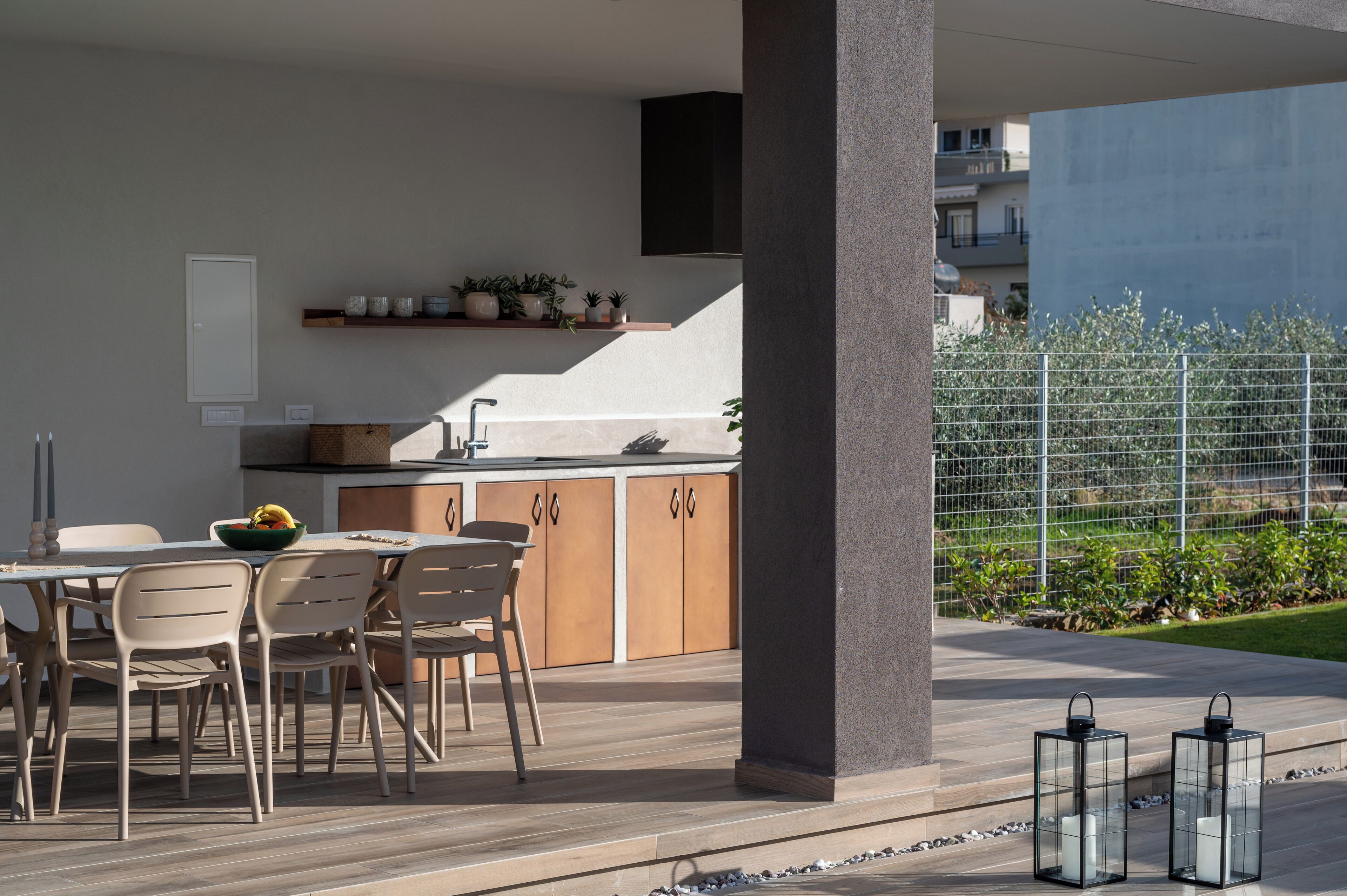 A modern outdoor kitchen with a dining area, wooden cabinets, and a built-in shelf with plants.
