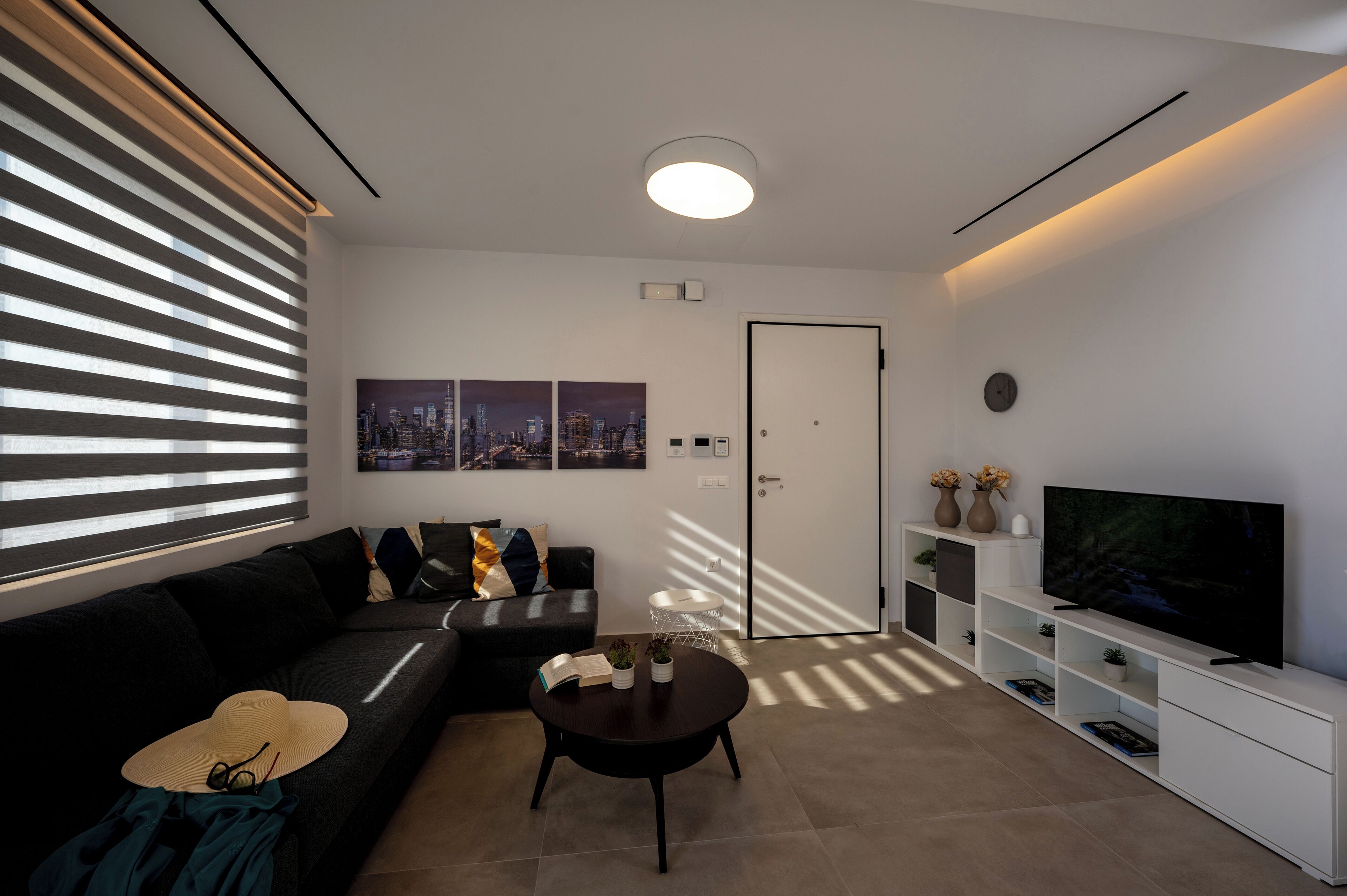 A modern living room with a black sofa, a round coffee table, a flat-screen TV, and a white entertainment unit.