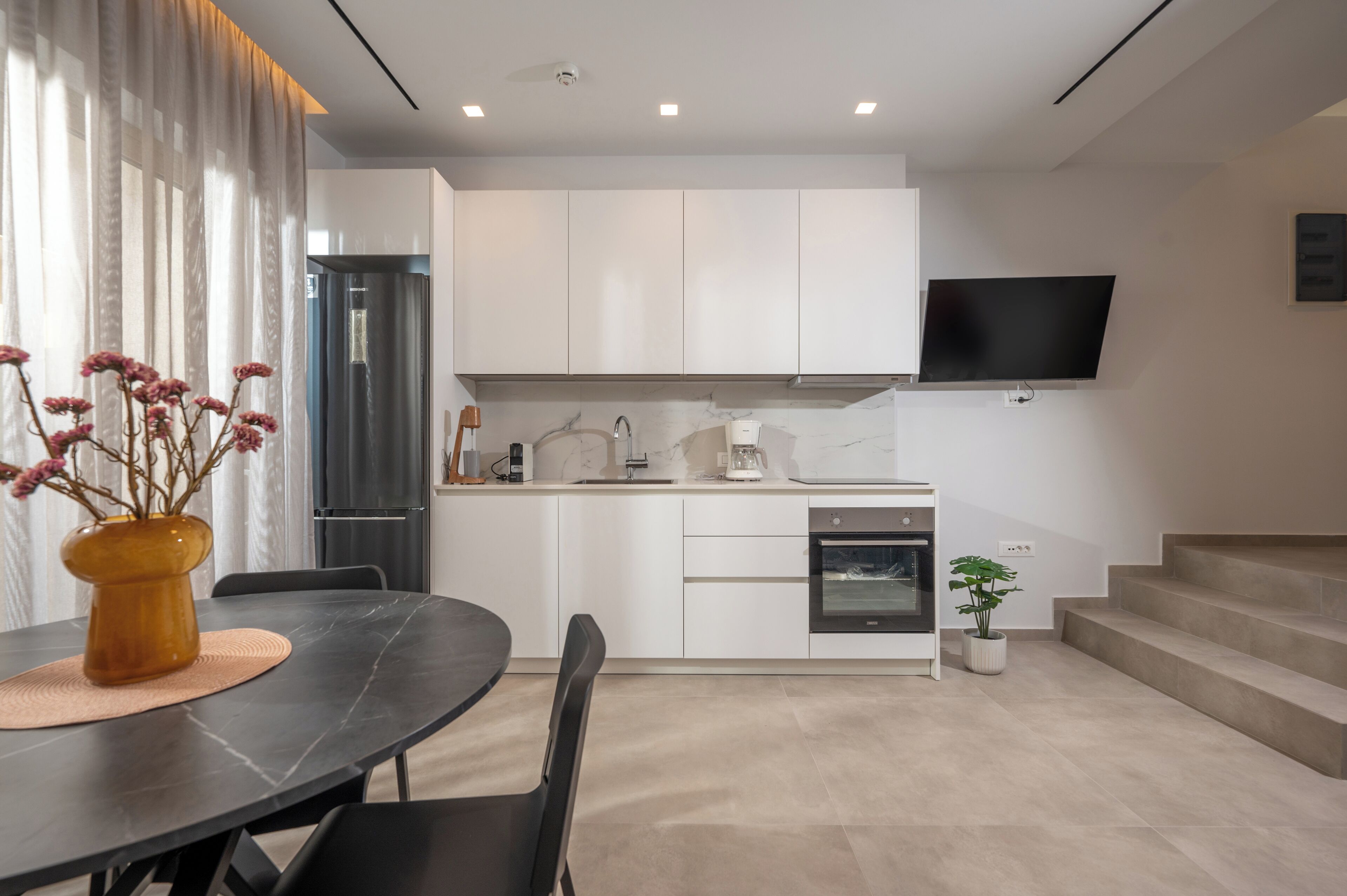 A modern kitchen with white cabinets, a built-in oven, and a flat-screen TV mounted above the counter.
