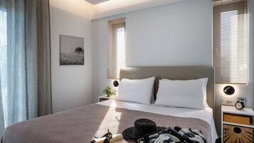A neatly made bed with white linens, a bedside table with a lamp, and a wall-mounted clock.