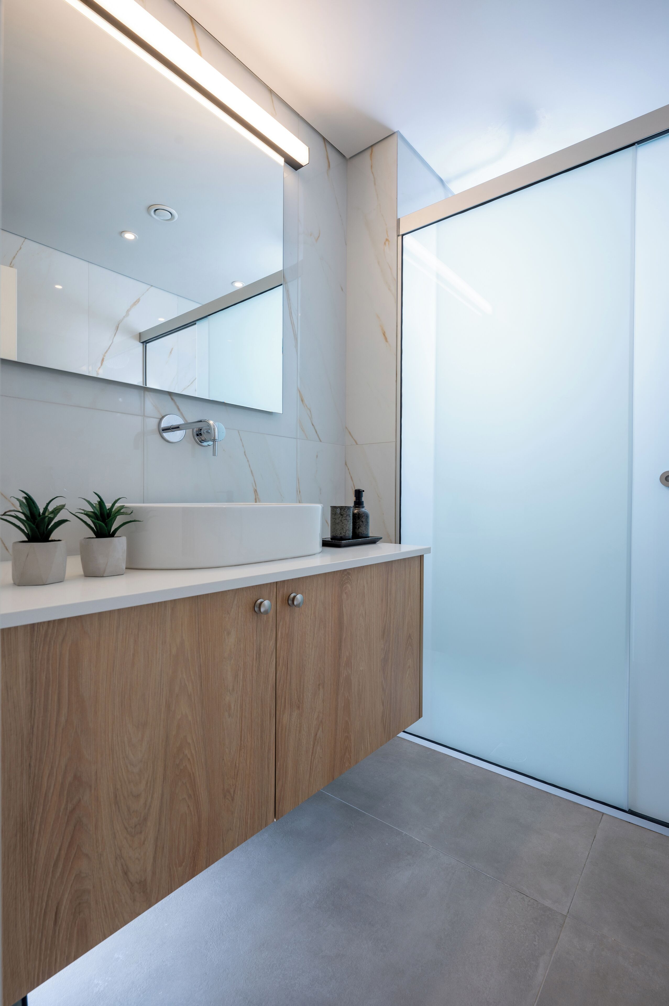 Une salle de bain moderne avec un grand miroir, un meuble-lavabo en bois, un lavabo blanc et une cabine de douche en verre.