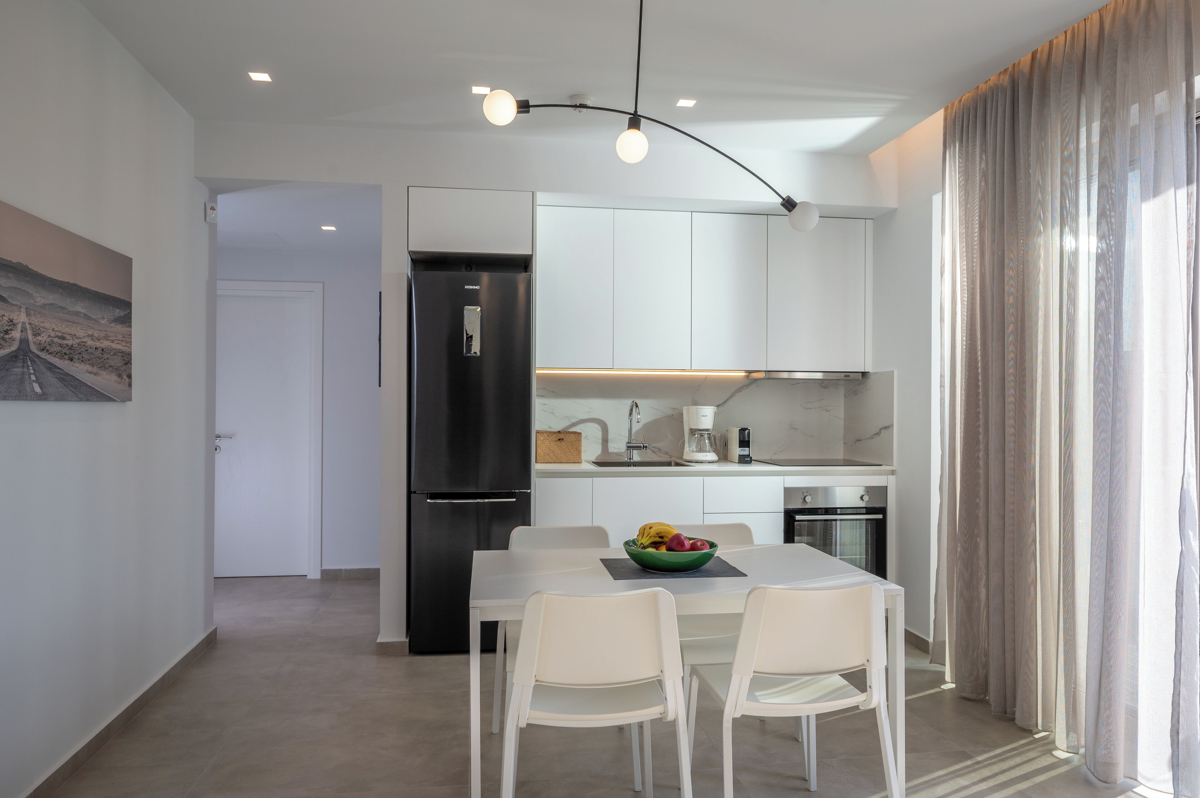 A modern kitchen with white cabinets, a black refrigerator, and a dining area with a white table and chairs.