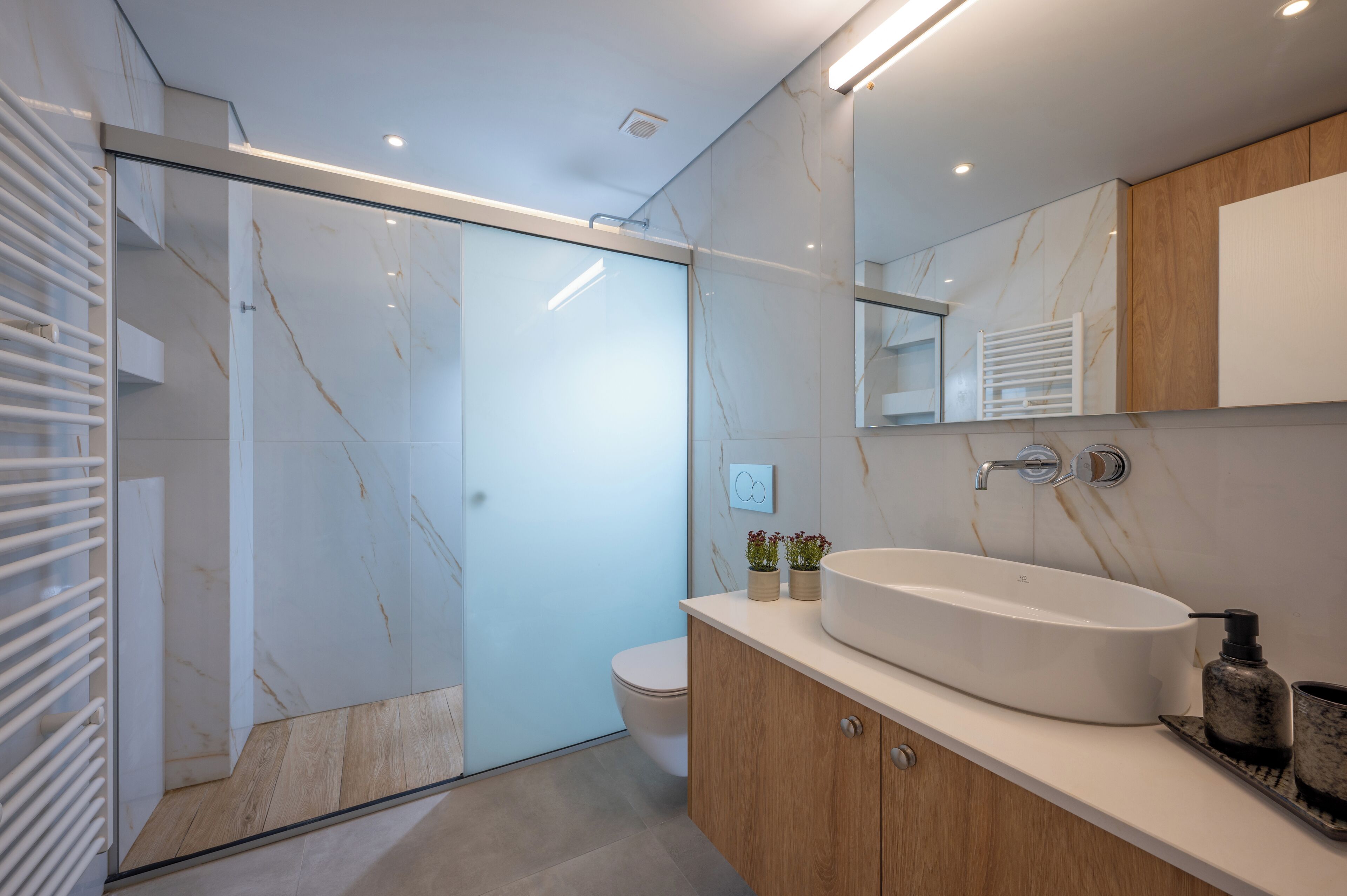 A modern bathroom with a glass shower enclosure, a white sink, and wooden cabinets.