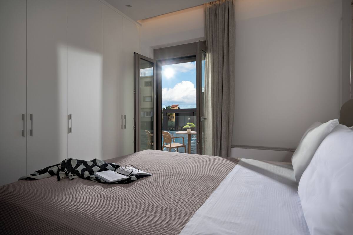 A hotel room with a bed, a desk, and a view of a balcony with a pool.