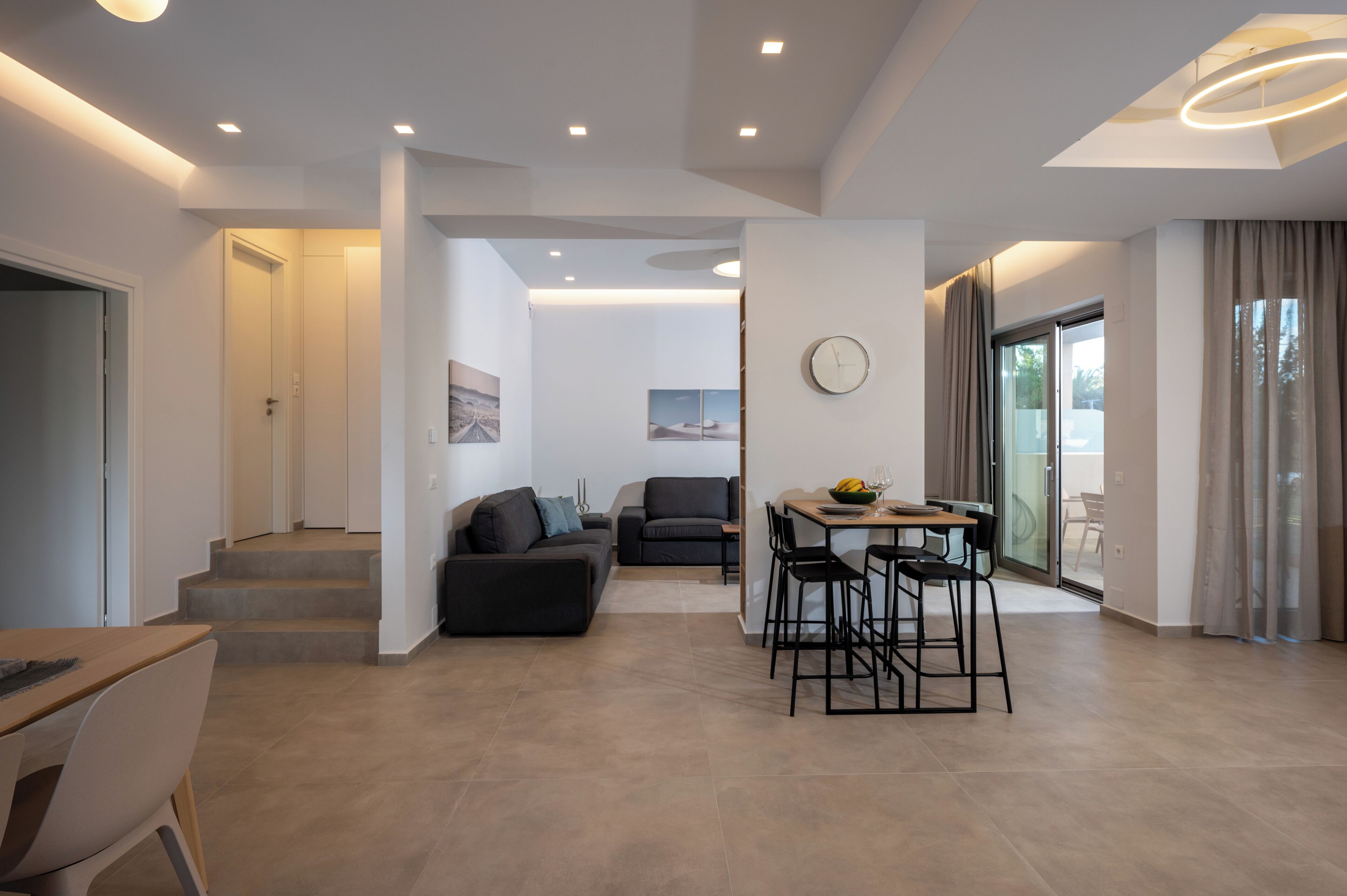 A modern living room with a dining area, a staircase, and a view of the outdoors.