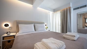 A neatly made bed with a headboard, a bedside table with a clock, and a mirror on the wall.