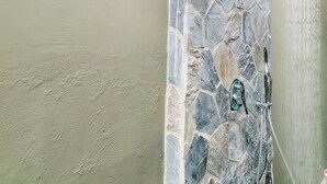 A stone wall with a showerhead, a yellow wall, and a red flower in the background.