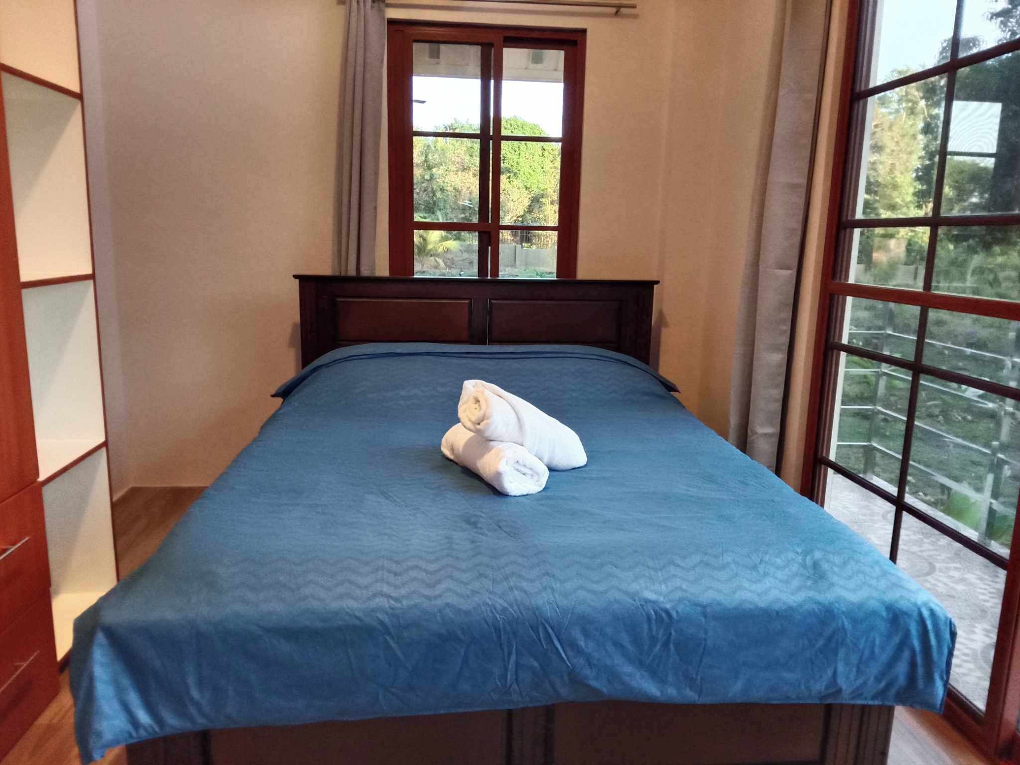 Une chambre avec une grande fenêtre, un lit recouvert d’une courtepointe bleue et une paire de serviettes posées sur le lit.
