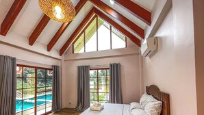 Een slaapkamer met een groot bed, houten balken, een plafondlamp en uitzicht op een zwembad.