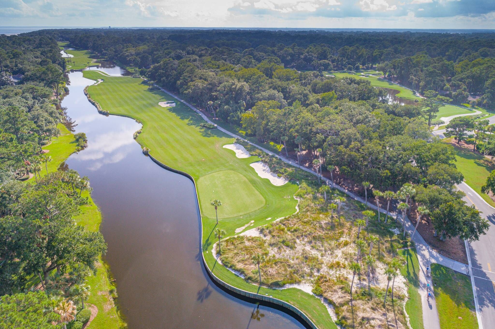 Luchtbeeld van een golfbaan met een waterpartij, zandbunkers en dichte bomen.