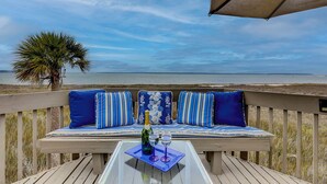 A wooden deck with a cushioned seating area overlooking a beach.