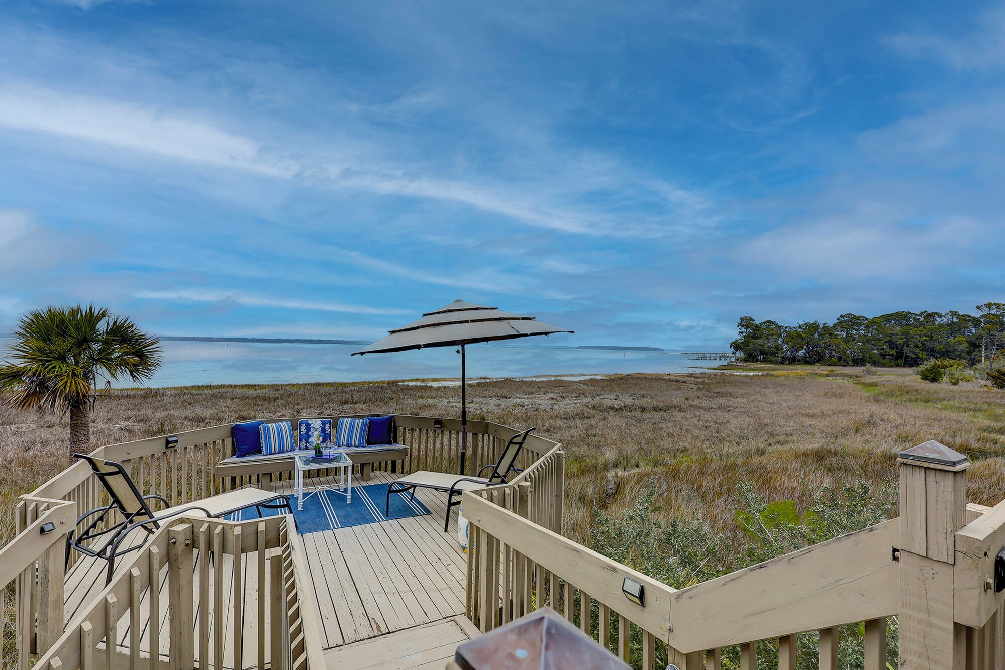 Una terraza de madera con un banco y una sombrilla, con vista a la playa y al agua.