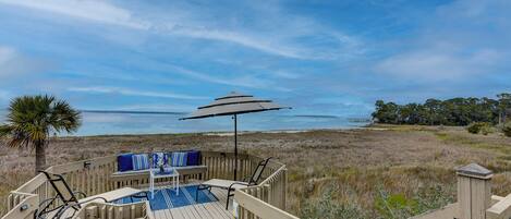 Una terraza de madera con un banco y una sombrilla, con vista a la playa y al agua.