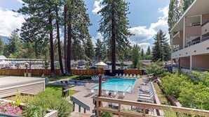 A pool area with lounge chairs, a wooden deck, and tall trees in the background. - Lakeland Getaway Walk to Lake! (South Lake Tahoe)