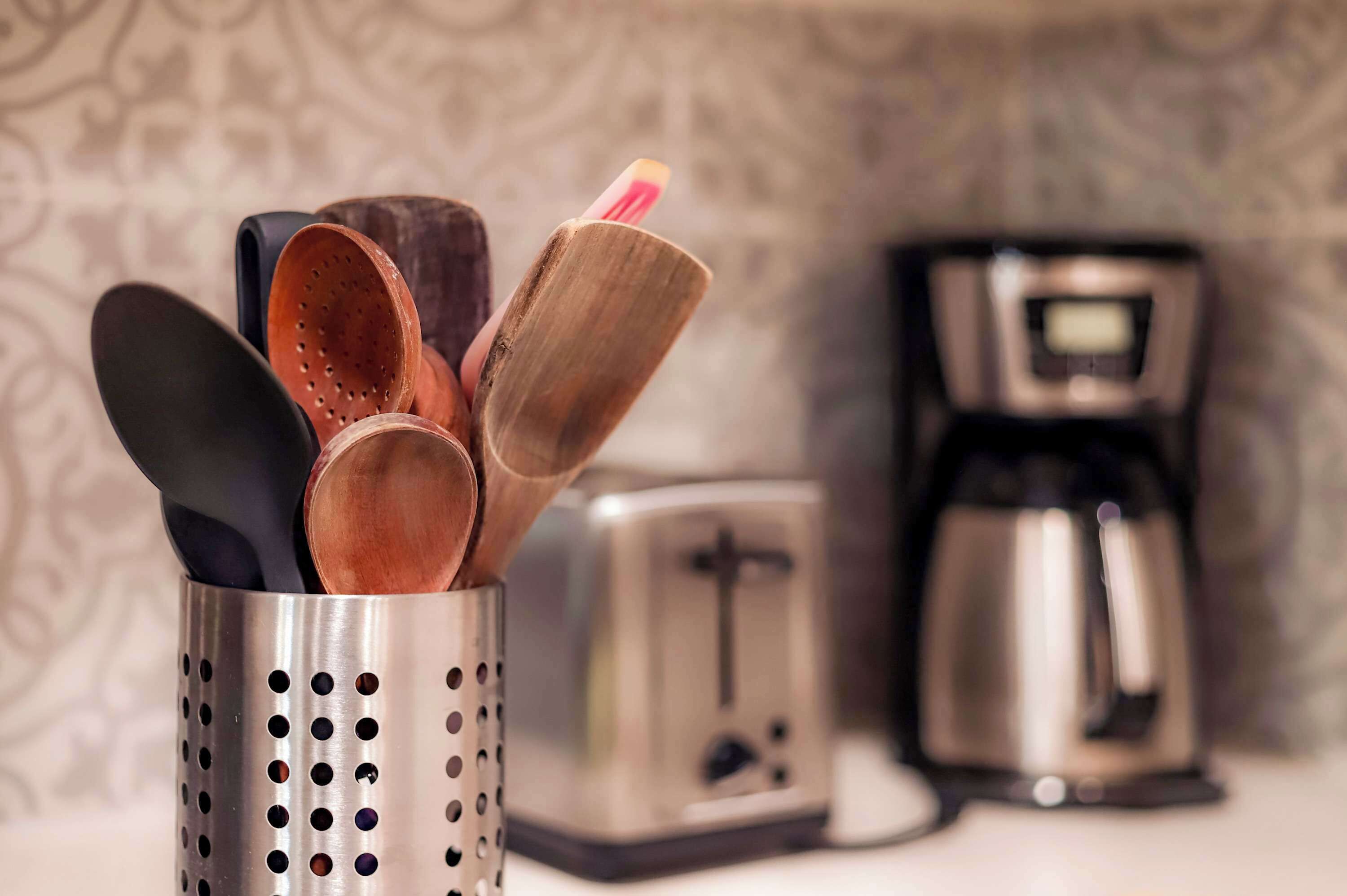 A kitchen with a metal utensil holder containing wooden spoons and a black spatula, a toaster, and a coffee maker.